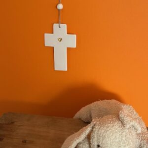 Croix latine en porcelaine non émaillée avec coeur en or accrochée dans une chambre d'enfant